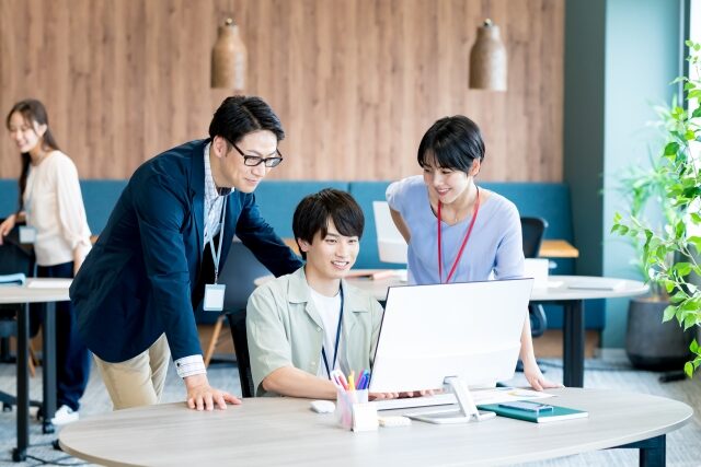オフィスでパソコン画面を一緒に見ている3人のスタッフ